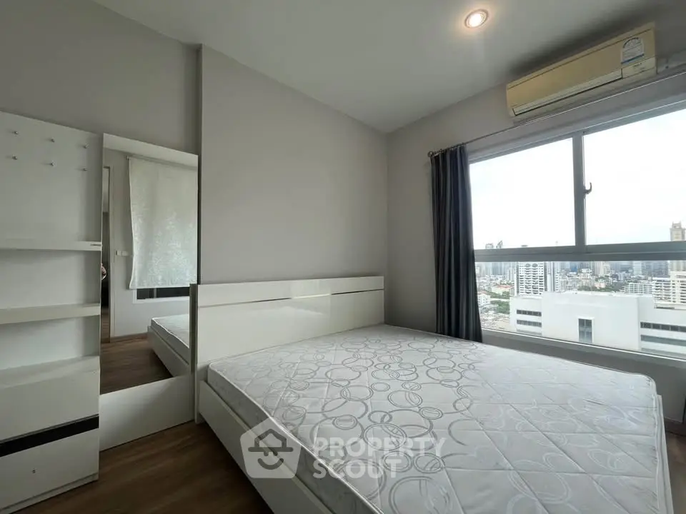 Modern bedroom with city view, featuring a large window and air conditioning unit.
