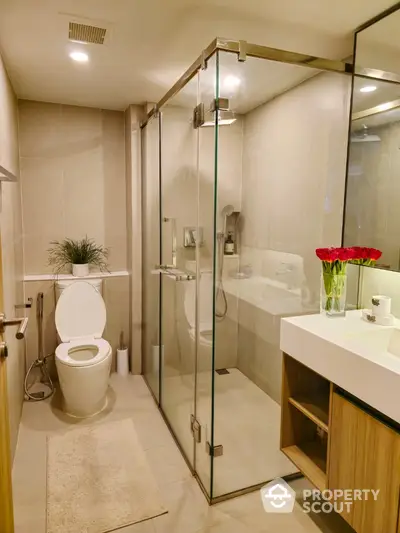 Modern bathroom with glass shower enclosure, sleek fixtures, and elegant vanity unit, accented by vibrant red flowers for a touch of color.