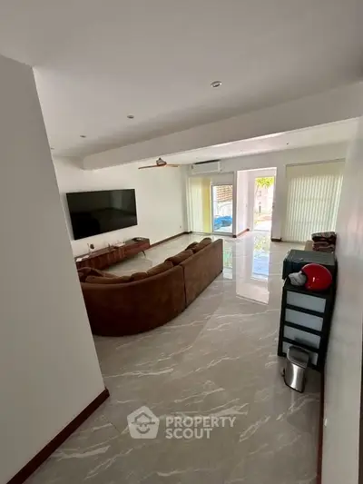 Spacious living room with modern decor and large TV, featuring a cozy brown sofa and pool view.