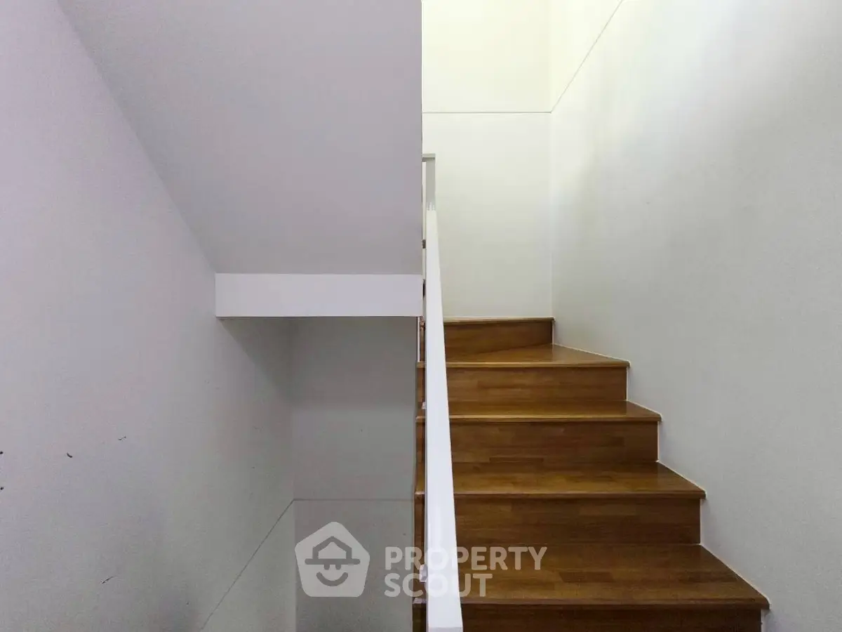 Modern wooden staircase with sleek white railing in a minimalist home interior.