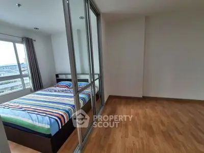 Spacious bedroom with large window and mirrored closet doors, featuring a colorful striped bedspread.