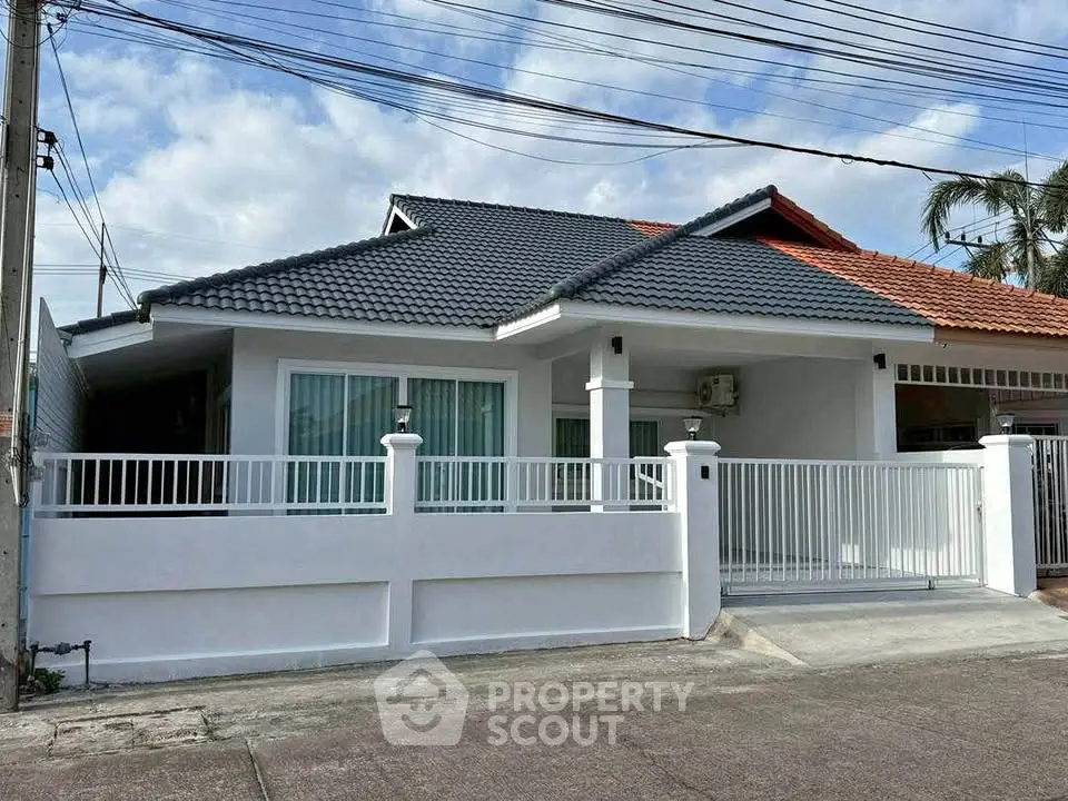 Charming single-story house with modern roof and white fence in a serene neighborhood.