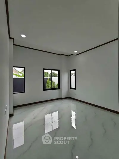 Spacious empty room with glossy marble flooring and large windows offering natural light.