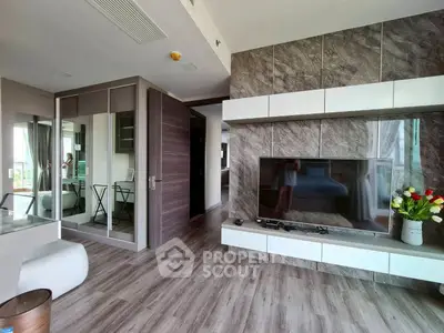 Modern living room with stylish decor and large TV, featuring elegant wood flooring and sleek storage solutions.