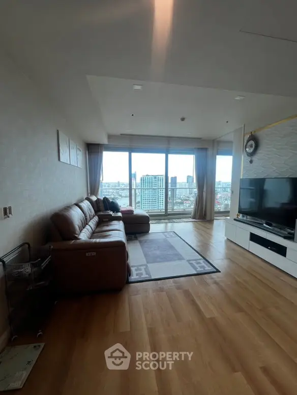 Spacious living room with large windows offering stunning city views, featuring modern furniture and wooden flooring.