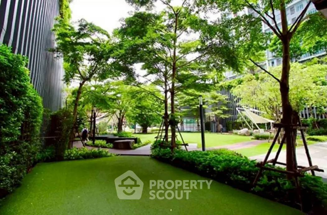 Lush green garden area in modern residential complex with trees and seating areas.