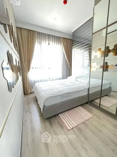 Modern bedroom with mirrored wardrobe and large window, featuring elegant decor and natural light.