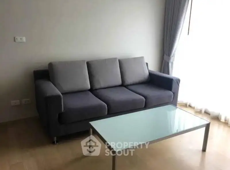 Modern living room with sleek gray sofa and glass coffee table, bathed in natural light.
