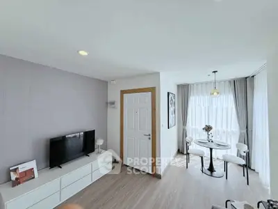 Bright modern living room with TV and dining area, featuring large windows and stylish decor.