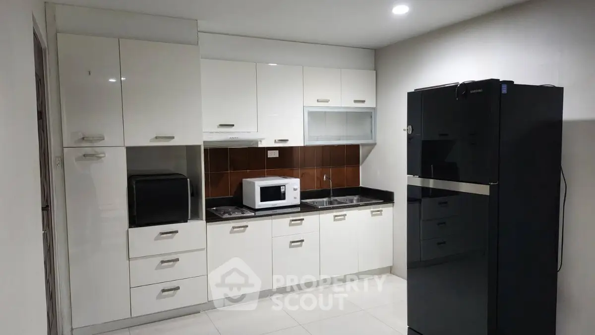 Modern kitchen with sleek cabinets, microwave, and refrigerator in a contemporary apartment.