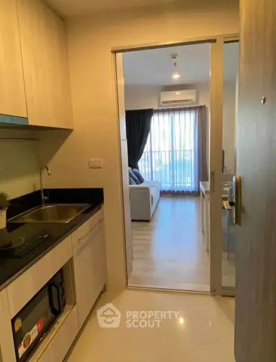 Modern apartment kitchen with open layout leading to a bright living room with large windows.