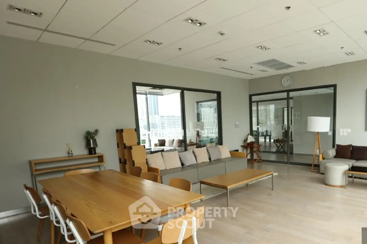Spacious modern living room with wooden furniture and large windows offering city views.