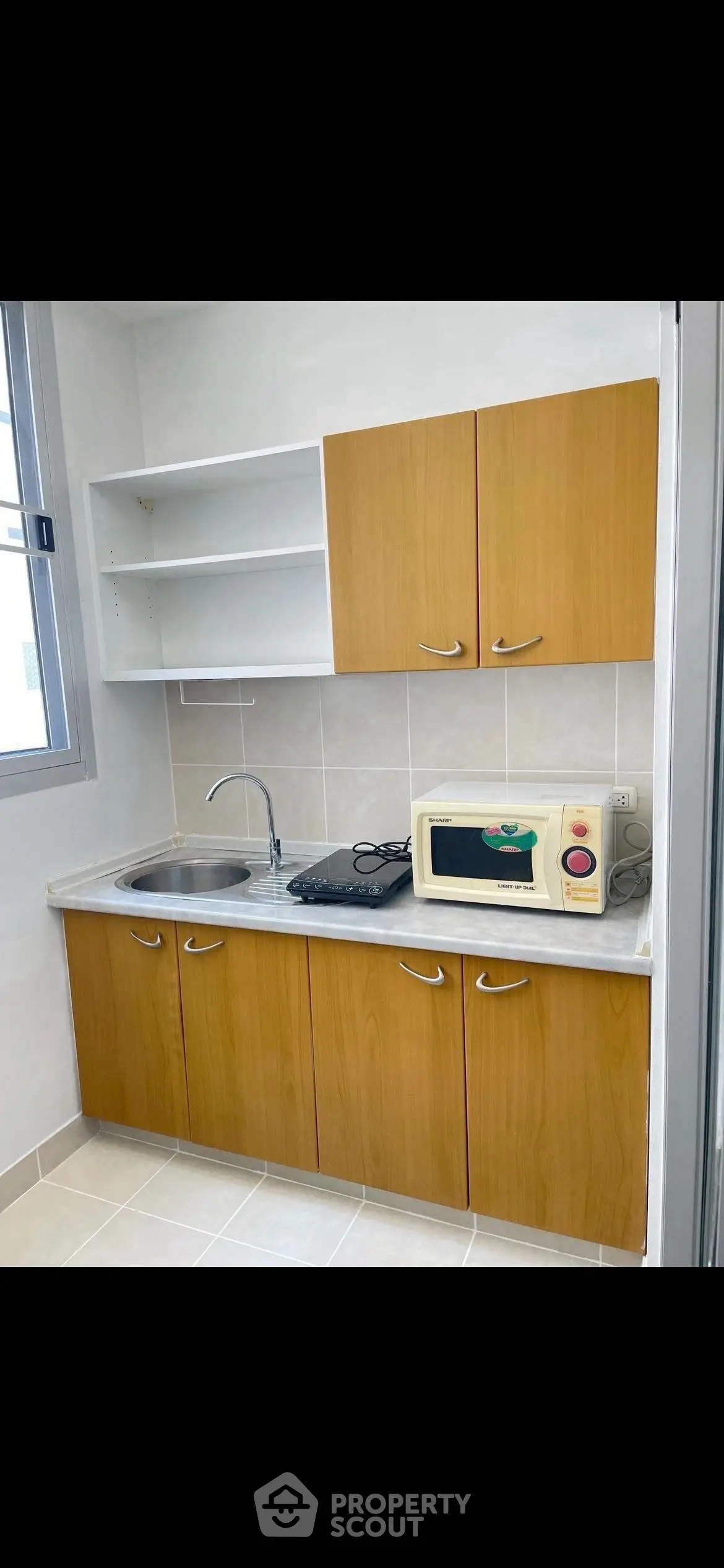 Compact kitchen with wooden cabinets, microwave, and electric stove in modern apartment.