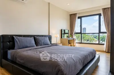 Spacious bedroom with large window and modern furnishings, offering a serene view.