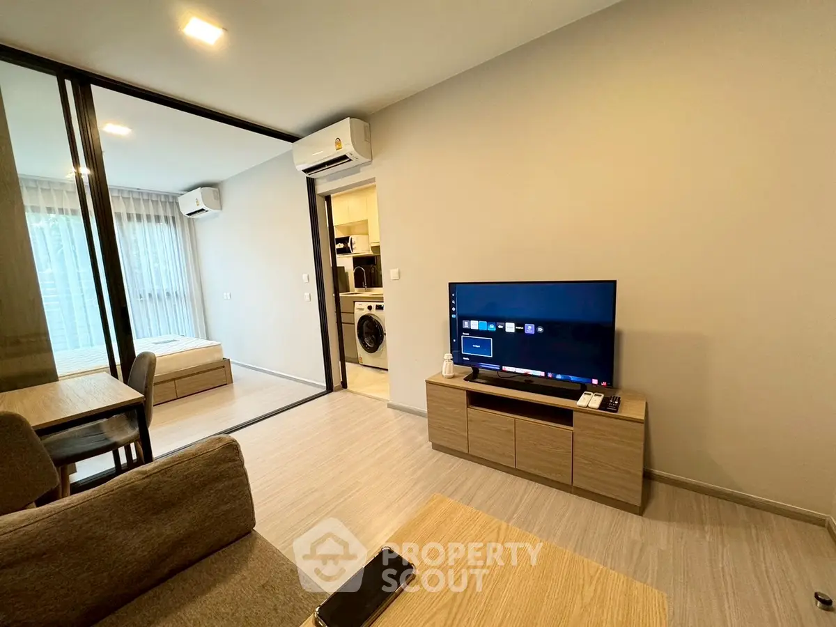 Modern living room with TV and view into bedroom, featuring sleek design and natural light.