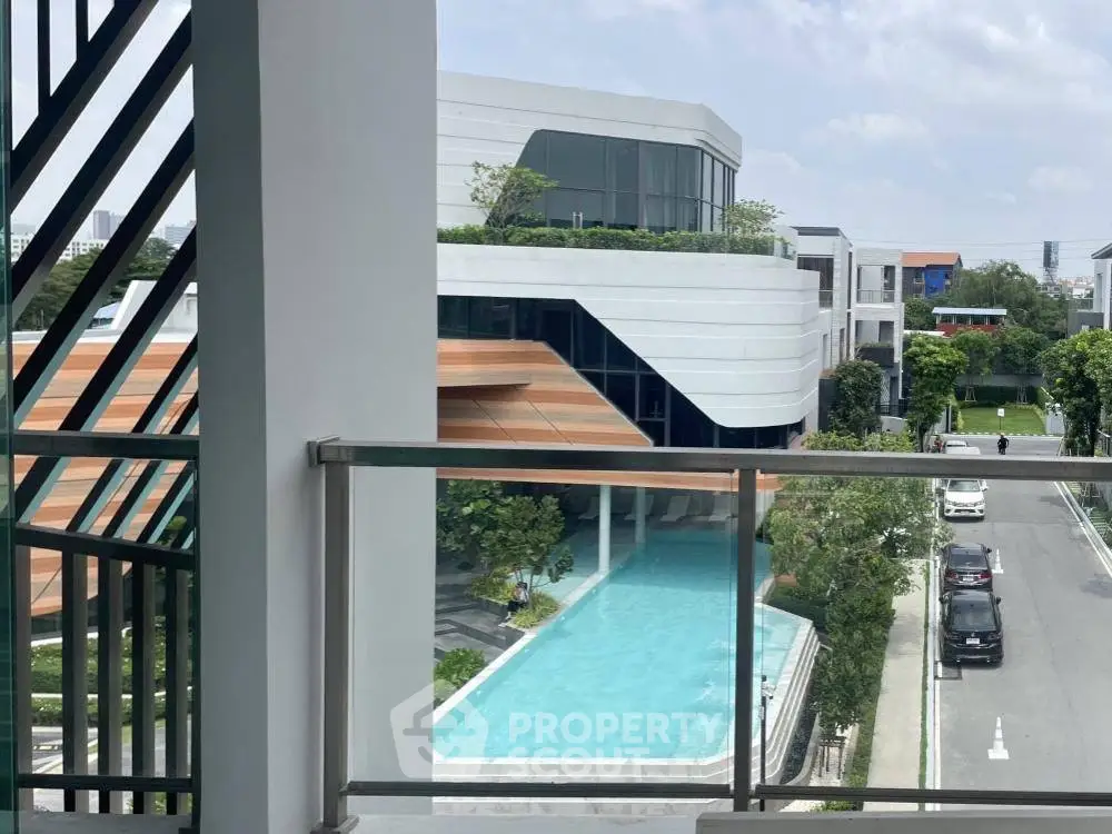 Modern building with pool view from balcony, showcasing sleek architecture and lush surroundings.