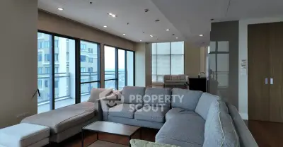 Spacious modern living room with large windows and city view, featuring a stylish gray sectional sofa.