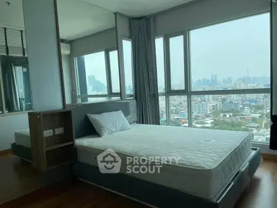 Spacious bedroom with panoramic city view and modern furnishings in high-rise apartment.