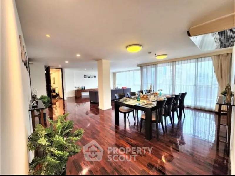 Spacious open-plan living and dining area with elegant wooden flooring and large windows.