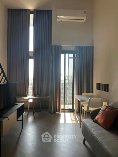 Modern living room with high ceilings and natural light, featuring a cozy sofa and sleek furniture.