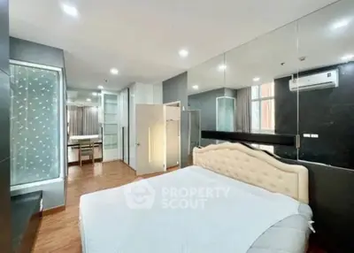 Spacious modern bedroom with mirrored wall and ensuite bathroom in luxury apartment.
