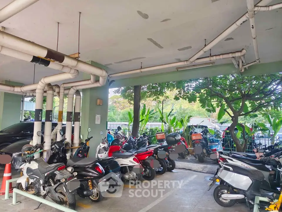 Covered parking area with multiple motorcycles and scooters, surrounded by lush greenery.