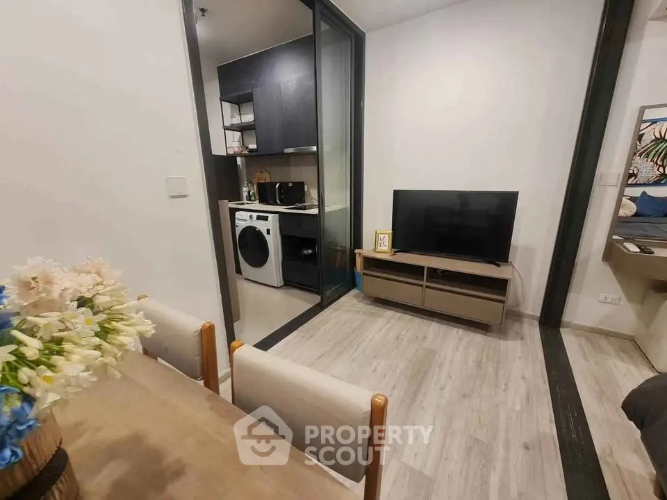 Modern apartment interior with open living space and kitchen featuring washing machine and TV setup.