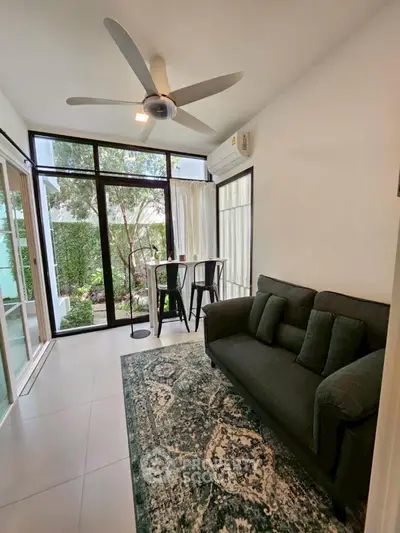 Chic living room with garden view, modern sofa, and ceiling fan in a bright, airy space.