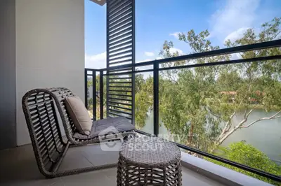 Charming balcony with wicker furniture overlooking serene river and lush greenery, perfect for relaxation.