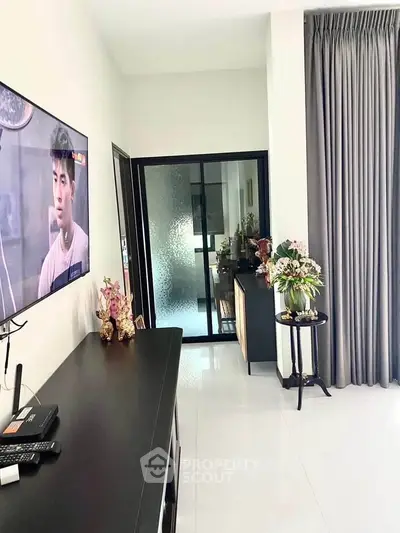 Modern living room with sleek decor and large TV, featuring elegant curtains and stylish furnishings.