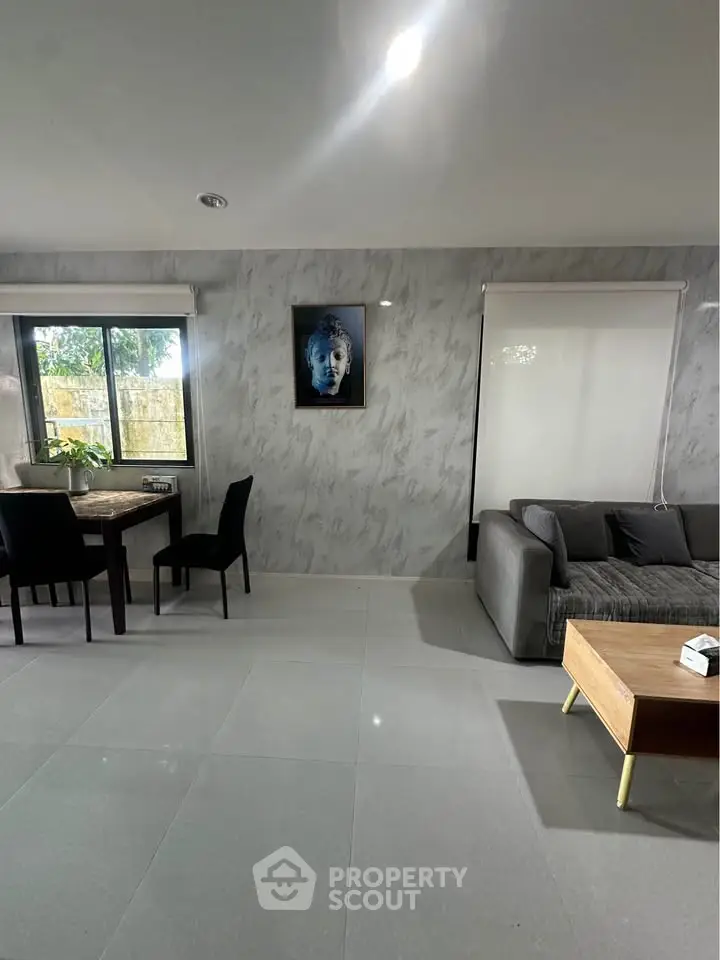 Modern living room with sleek furniture and Buddha artwork, featuring large windows and elegant decor.