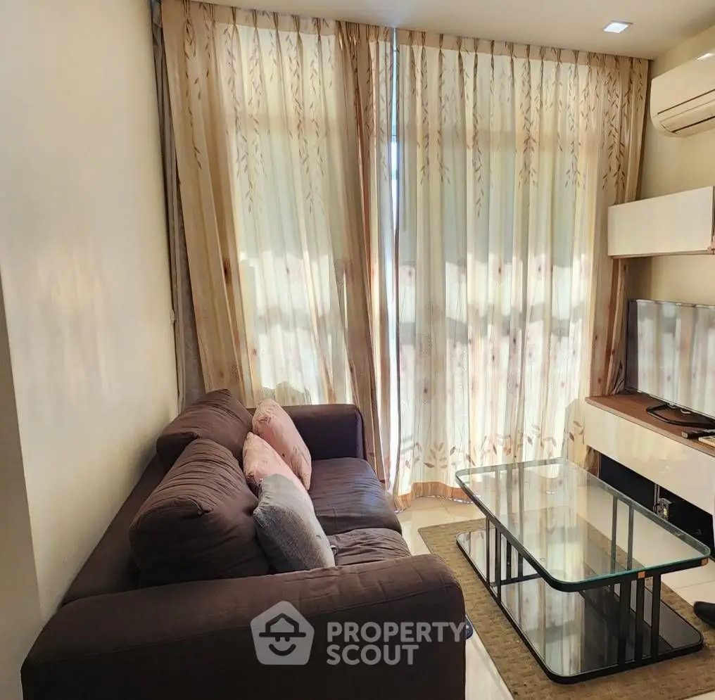 Cozy living room with plush sofa, glass coffee table, and elegant curtains.