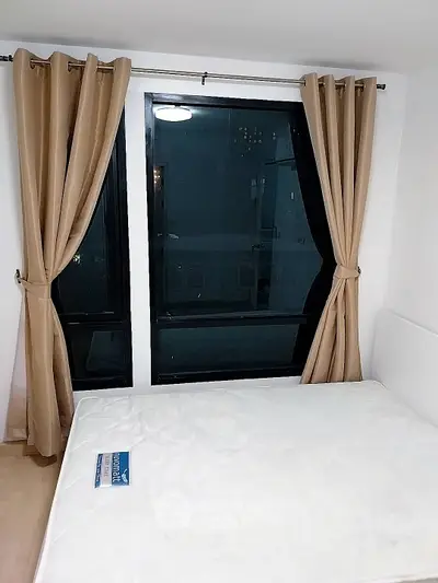 Cozy bedroom with large window and beige curtains, perfect for natural light.