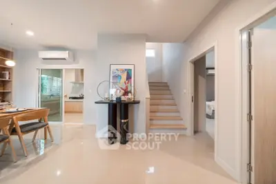 Modern open-plan living space with dining area and staircase, featuring sleek design and natural light.
