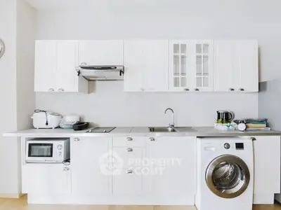 Modern kitchen with white cabinetry, washing machine, and microwave in a sleek open layout.