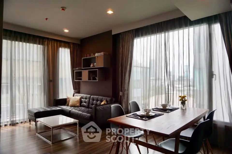 Modern living room with large windows and stylish dining area in a corner unit apartment.