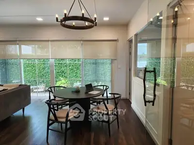 Elegant dining area with modern chandelier and large windows overlooking lush greenery.