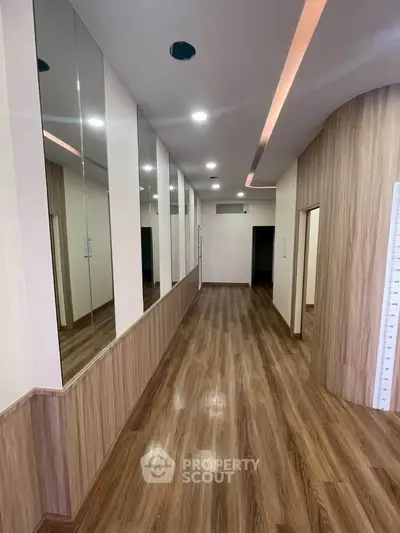 Sleek modern hallway with wood flooring and mirrored walls in a contemporary building.