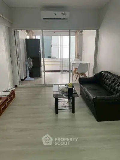 Modern living room with sleek black sofa and glass doors leading to a bright balcony area.