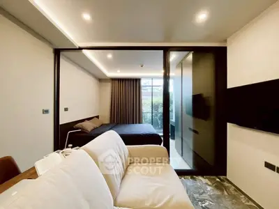 Modern living room with cozy sofa and stylish bedroom separated by glass partition, featuring elegant lighting.
