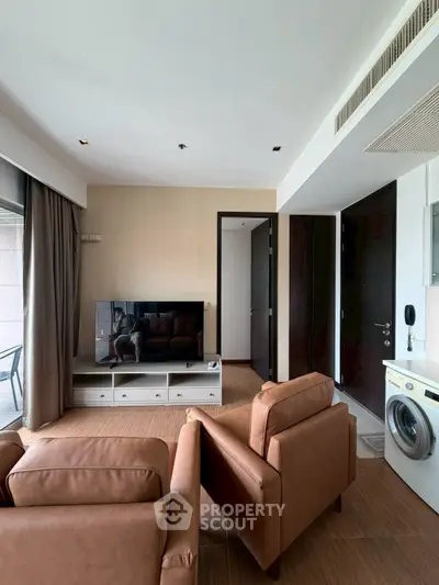 Modern living room with leather chairs, TV, and washing machine in a stylish apartment.
