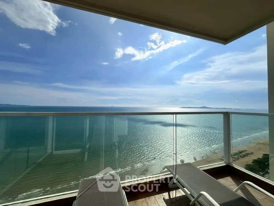 Stunning ocean view from a high-rise balcony with glass railing and lounge chairs.
