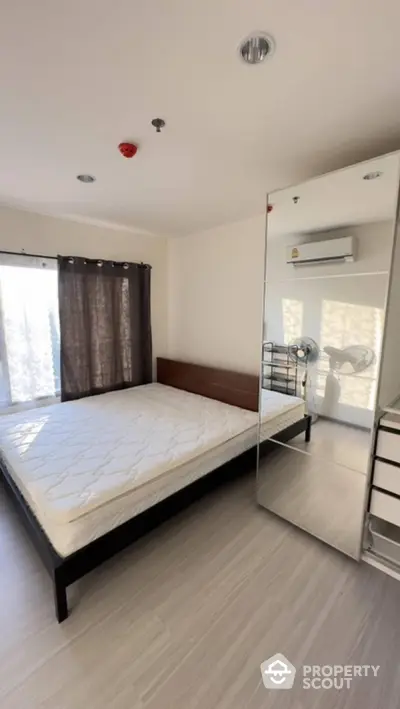 Modern bedroom with large mirror and natural light, featuring minimalist design and air conditioning.