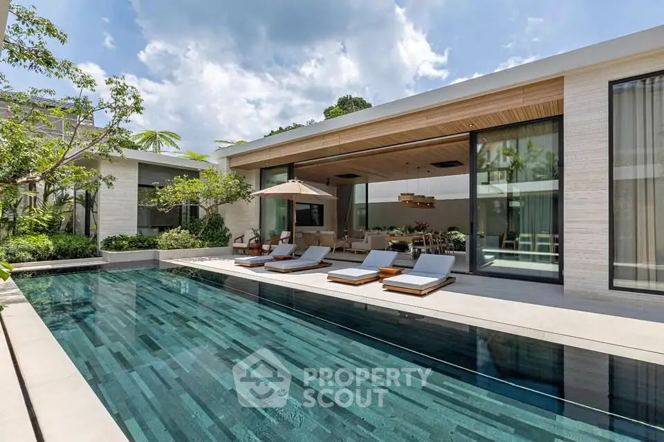 Luxurious modern villa with sleek pool and sun loungers, surrounded by lush greenery.
