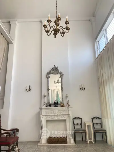 Elegant living room with high ceilings, chandelier, and ornate fireplace mirror.