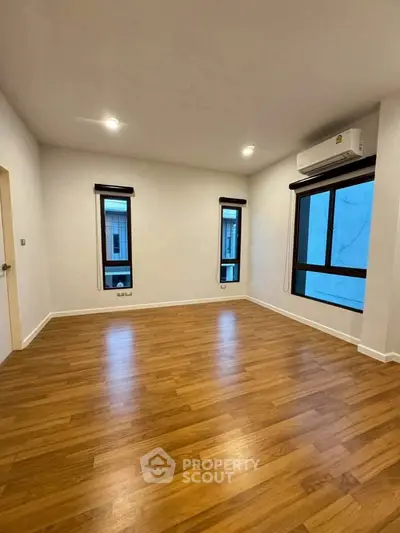 Spacious empty room with wooden flooring and large windows, perfect for customization.