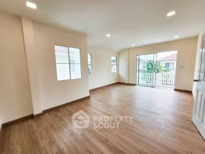 Spacious empty room with wooden flooring and large windows offering natural light.
