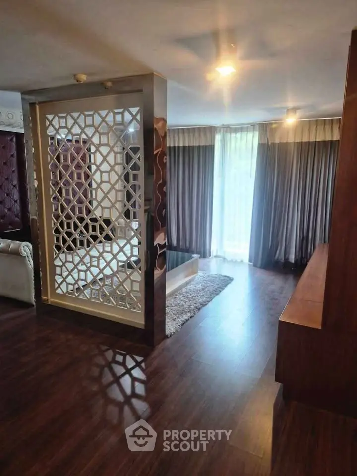 Elegant living room with wooden flooring and decorative partition, featuring large windows and luxurious curtains.