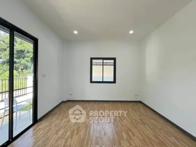 Spacious empty room with wooden flooring and large window, perfect for customization.