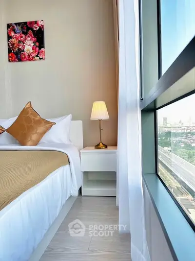 Modern bedroom with large window offering stunning city view, elegant decor, and cozy ambiance.